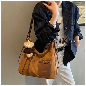 Brown suede hobo bag with teddy bear charm shown on a model in urban casual style