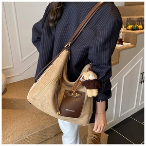 Detail of khaki suede tote bag with leather straps and teddy bear charm on model