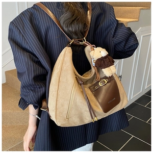 Detail of khaki suede hobo bag with teddy bear charm shown on model in modern office