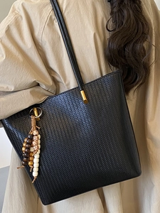 Grand sac cabas noir tressé avec détails dorés et pompon perlé porté sur un trench