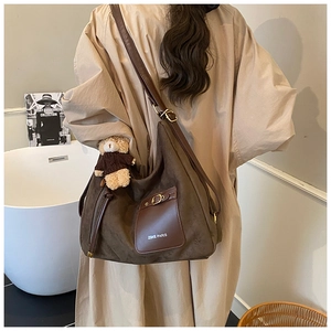 Detail of vintage brown suede tote bag featuring leather pocket and bear charm accessory