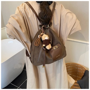 Close-up of brown frosted leather backpack detail featuring a cute teddy bear pendant