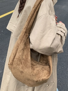 Brown suede hobo crossbody bag styled with a khaki trench coat in an urban street setting
