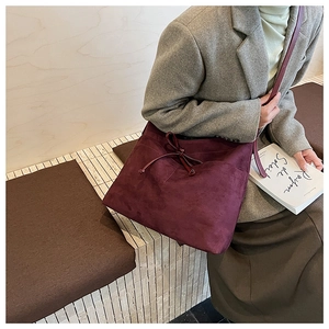 Détail du sac cabas bordeaux en daim avec nœud décoratif sur un mannequin en blazer gris