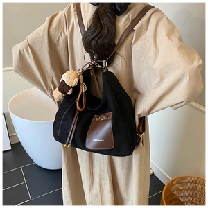 Detail of black canvas tote bag with brown leather pocket and cute bear charm accessory