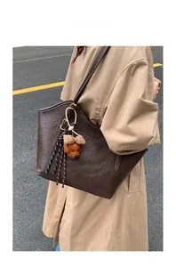Detail of dark brown tote bag with teddy bear charm on camel trench coat model