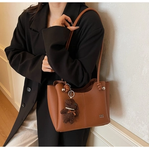 Sac cabas marron avec breloque ours porté à l'épaule par un mannequin sur fond blanc