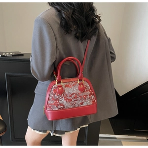 Detail of red shell bag with floral embroidery and golden hardware worn over a grey blazer