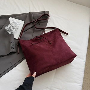 Gros plan du sac cabas en daim bordeaux avec un nœud décoratif et une surface texturée