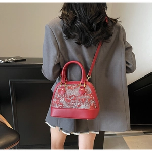 Detail of red shell-shaped handbag with white floral embroidery and gold hardware