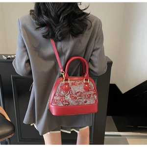 Detail of red and white shell bag with phoenix embroidery worn with a grey blazer