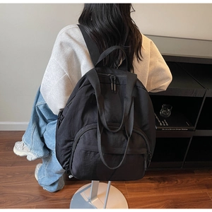 Rear view of model wearing a lightweight black nylon backpack with double zippers
