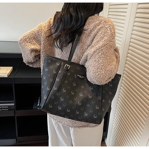 Détail du sac cabas noir avec motif floral d'élan et plaque de logo en métal doré