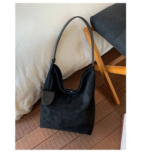 Detail of black suede hobo bag featuring knotted shoulder strap and circular pendant