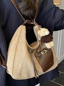 Large beige shoulder bag with brown leather pocket worn by a model in a navy blazer