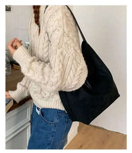 Detailed view of large black suede shoulder bag worn with a beige sweater