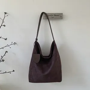 Detailed texture of a dark brown suede hobo bag hanging on a minimalist metal hook