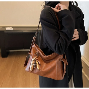 Close-up of brown textured leather crossbody bag featuring unique beaded tassel detail