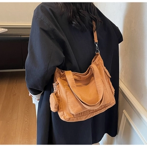 Detail of tan canvas tote bag with adjustable shoulder strap on a model wearing dark coat