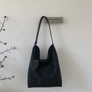 Detail of minimalist black suede hobo bag with long shoulder strap and decorative tag