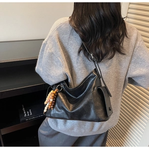 Close-up of black leather crossbody dumpling bag featuring decorative colorful wood beads
