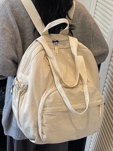 Minimalist beige large capacity backpack with multiple pockets shown from a side-back view