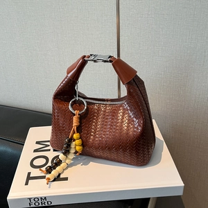Detail of red-brown woven hobo bag with silver buckle on a Tom Ford book