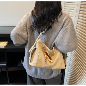 Detail of beige hobo bag with wooden bead charm and side pocket on a model's shoulder