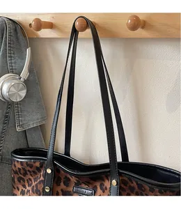 Detail of leopard print tote bag featuring metallic fashion logo and black leather straps