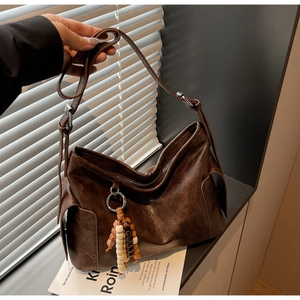 Detail of vintage dark brown dumpling bag with decorative wooden bead tassel and smooth PU texture