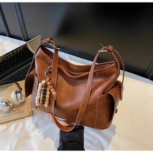 Close-up of brown faux leather tote bag with wooden bead tassel and side flap pockets