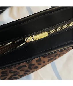Detailed close-up of the smooth gold metal zipper on leopard print tote bag with black trim