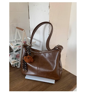 Détail du sac cabas en cuir marron foncé brillant avec coutures croisées et ours en peluche