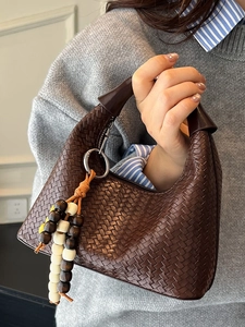 Brown woven leather hobo handbag with a long wooden bead charm and half-moon silhouette