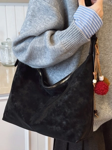 Große schwarze Hobo-Tasche aus Wildleder mit Anhängern in einem lässigen Lifestyle-Ambiente