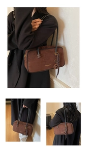 Detail of brown suede shoulder bag showing gold brand logo and decorative tassel ornament