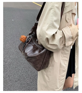 Grand sac cabas rétro en cuir marron foncé avec pendentif ours sur un trench-coat beige