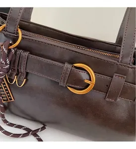 Détail d'un sac en cuir marron vintage avec anneaux dorés et breloque décorative