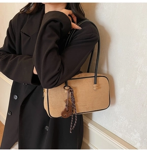 Detail of khaki suede shoulder bag featuring slim black handles and decorative charms
