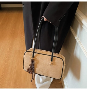Detail of apricot suede tote with black leather trim and woven pendant on a model