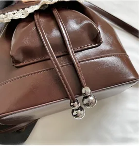Detail of dark brown faux leather bag featuring lace trim and silver metallic bead tassels