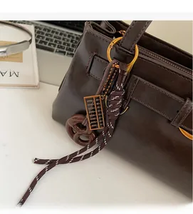Gros plan du sac en cuir marron avec breloque boulier et nœud en corde tressée