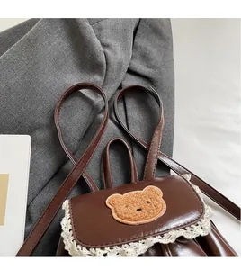 Detail of vintage brown mini backpack featuring a plush bear patch and lace trim