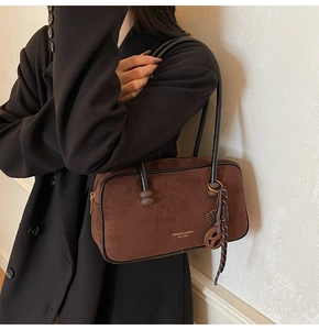 Detail of dark brown suede shoulder bag with black strap and metallic zipper closure