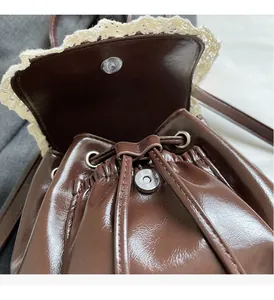 Detail of brown wax leather bag featuring white lace trim and silver magnetic buckle