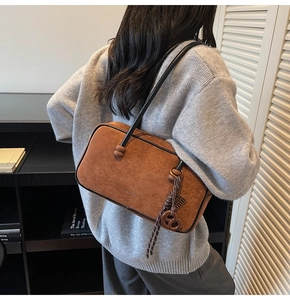 Detail of vintage brown suede shoulder bag with pretzel charm and brand logo