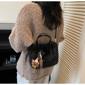 Détail du sac à main en fausse fourrure noire avec breloque ours sur un pull marron