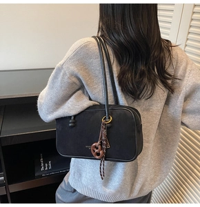 Detail showing matte black rectangular shoulder bag with brown bow charm accessory