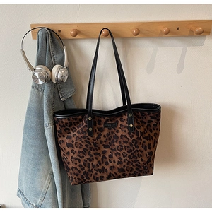 Detail of leopard print tote bag with rivets and brand label on a wooden wall hook