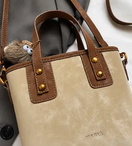 Dettaglio borsa a secchiello in camoscio beige con manici in pelle e borchie dorate